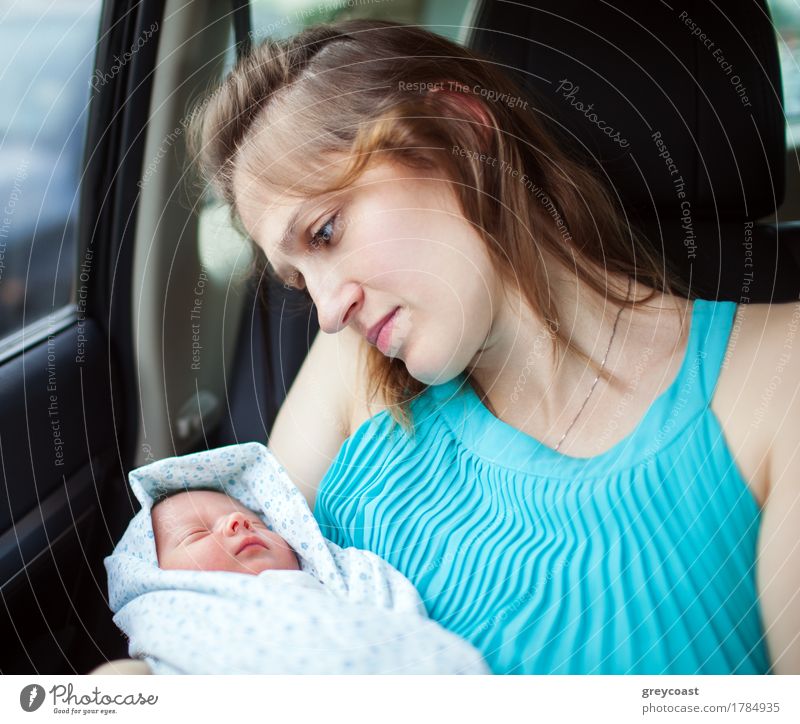 Young mother holding newborn wrapped in baby blanket while sitting in the car. Woman looking at her baby with deep feelings expressed in the eyes Child Baby