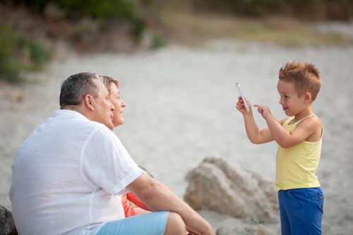Smiling little child with smart phone taking picture of happy grandmother and grandfather. Family leisure outdoor Happy Summer Beach Child Telephone PDA Camera