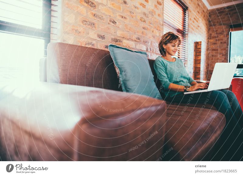 Mature woman sitting on couch at modern home Lifestyle House (Residential Structure) Work and employment Profession Office Business Computer Notebook Technology