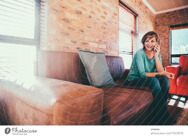 Happy mature woman talking on her smartphone Lifestyle Joy Living room Business To talk Telephone Cellphone PDA Technology Telecommunications Human being Woman