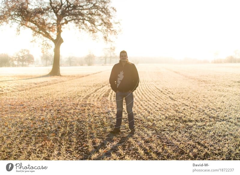 Man stands outside in the field in frost chill Frost Sunlight Sunbeam Sunset Light Yellow Arable land acre Frozen hands in the pockets Looking into the camera
