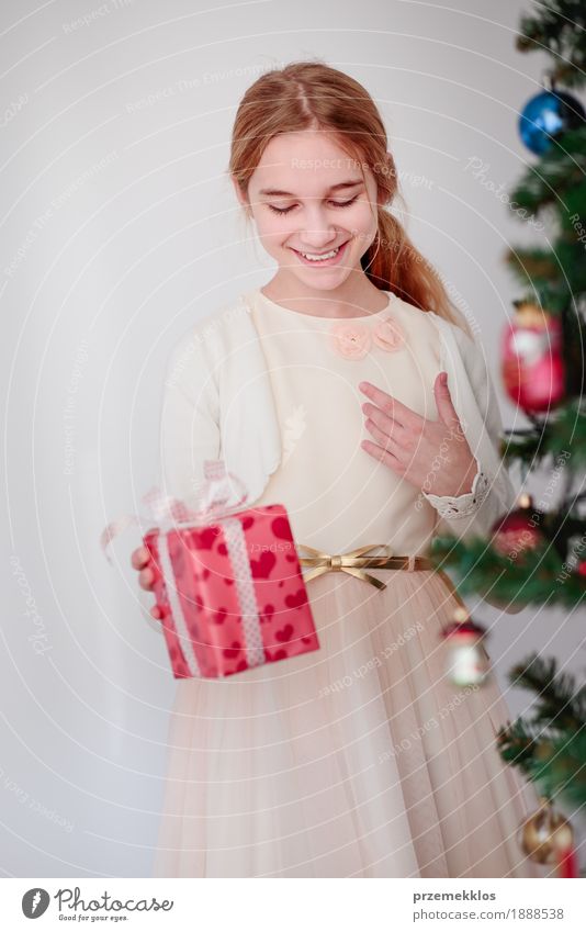 Happy girl holding Christmas gift standing behind a tree Lifestyle Feasts & Celebrations Christmas & Advent Child Human being Girl 1 8 - 13 years Infancy Tree