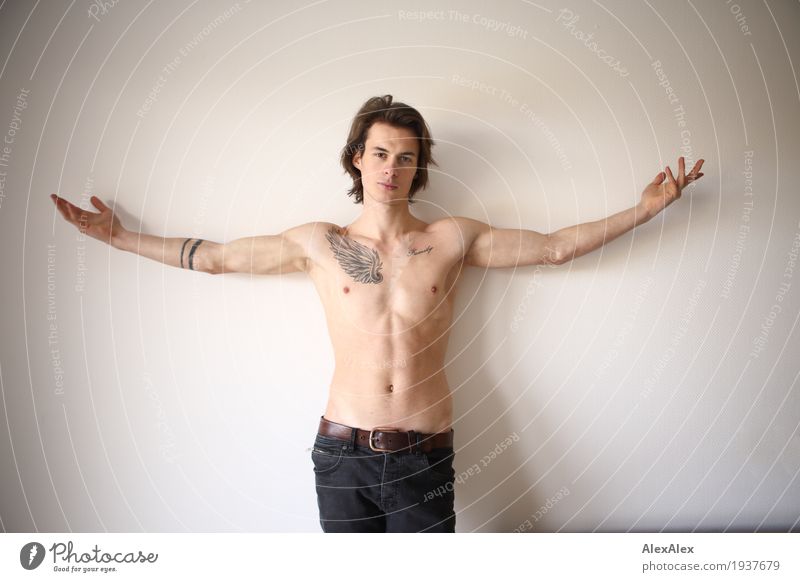 young man spreads his arms like an angel while leaning against the wall with a tattoo on his bare chest Style Joy Happy pretty Body Young man