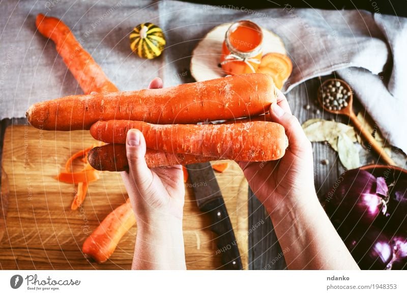 female human hand holding three large orange carrot Food Vegetable Herbs and spices Nutrition Vegetarian diet Diet Beverage Juice Table Kitchen Woman Adults