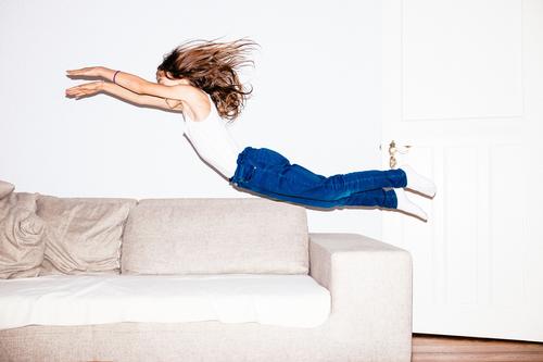 Long haired girl in jeans jumps headfirst into a sofa Feminine Child 8 - 13 years Infancy Jeans Brunette Long-haired Flying Jump Brash Happiness Infinity Funny