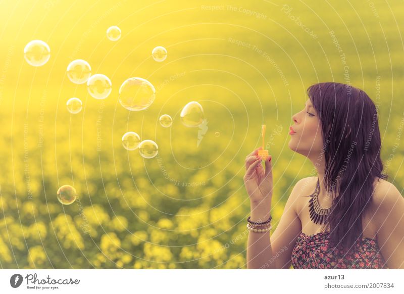 Beautiful young woman with soap bubbles in summer on yellow meadow from rape to horizon. Pretty girl with zest for life enjoying the sunshine break and life. Rest and recharge energy from time stress in the environment and nature idyll.