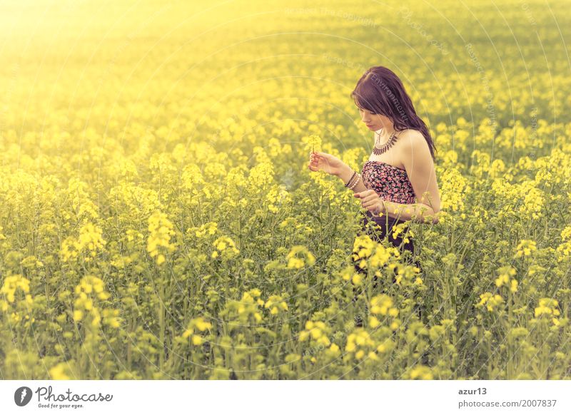 Beautiful young woman picking flowers in summer on yellow meadow from rapeseed to horizon. Pretty girl with zest for life enjoying the sunshine break and life. Rest and recharge energy from time stress in environment and nature idyll.