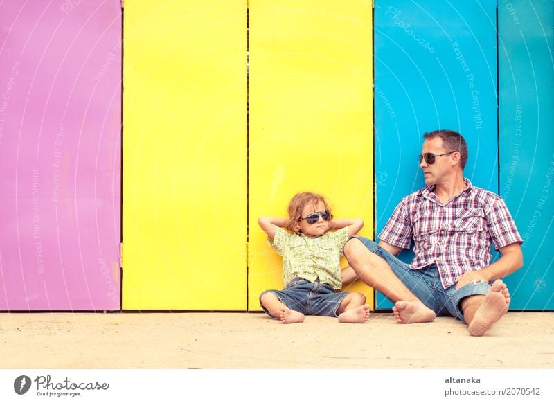 Father and son relaxing near the house at the day time. They sitting near are the colorful wall. Concept of friendly family. Lifestyle Joy Happy Relaxation