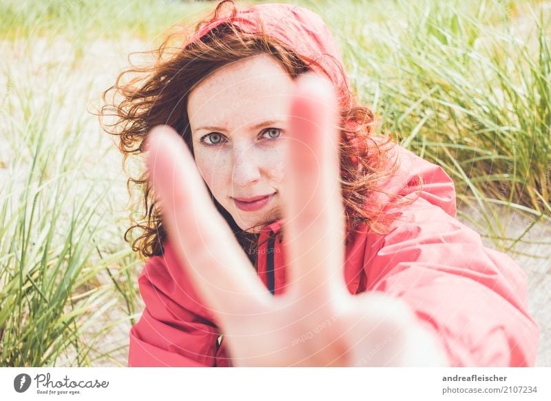 Young woman with windbreaker sits in the dune on the beach and shows the peace sign Lifestyle Vacation & Travel Tourism Trip Far-off places Freedom Summer