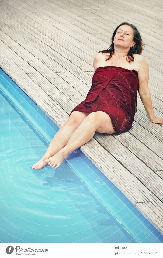 Mature brunette woman sunbathing by the pool with her feet in the water and a wrap around her body Water Woman wraparound garment Relaxation Summer