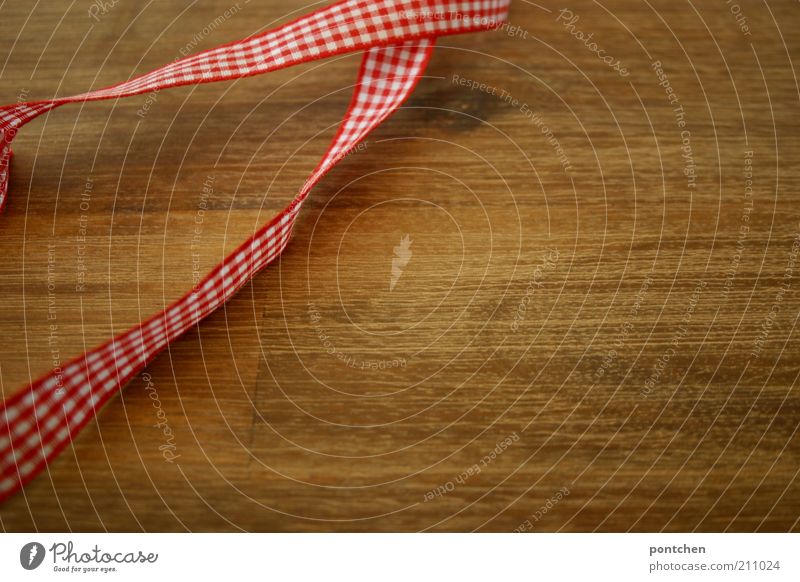A red and white chequered ribbon lies on a wooden table. Christmas, wrap it up, tie it up Style Design Handicraft Arrange Decoration Kitsch Odds and ends