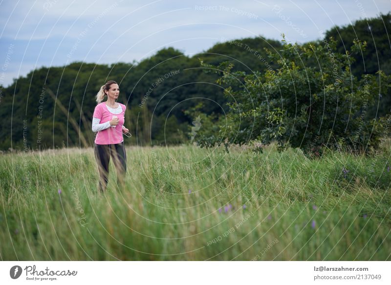Fit middle-aged woman running through a field Lifestyle Happy Summer Sports Jogging Telephone Cellphone Woman Adults Nature Lanes & trails Blonde Fitness