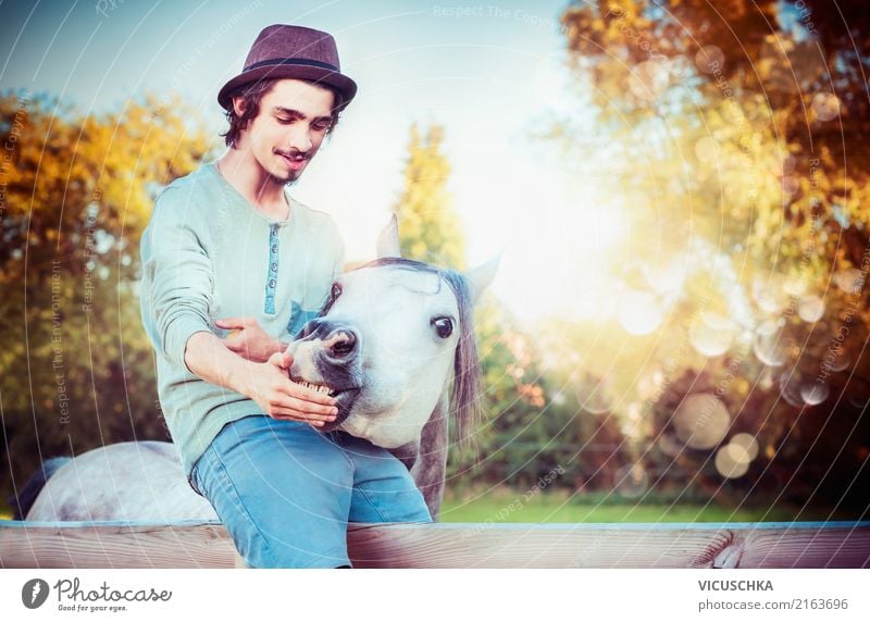 Young man sits on the fence and feeds horse Lifestyle Style Human being Youth (Young adults) 1 Nature Animal Horse Emotions Moody young Man Love of animals