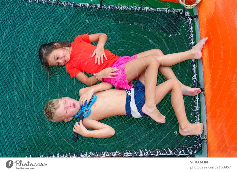 Cute kids on a boat trip. Boy is playing a toy guitar and sings for his beautiful girlfriend. Lying on catamaran's hammock, legs are intertwined. View from above
