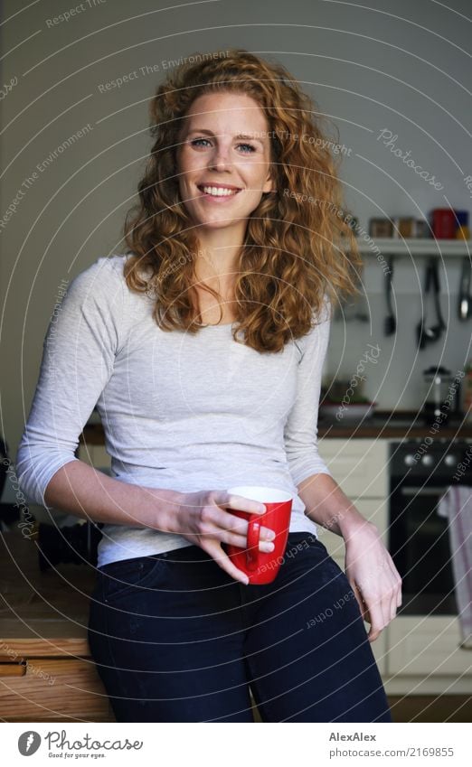 young redhead beautiful woman with curls and freckles in her kitchen with red cup in hand, smiling at camera Coffee Cup Kitchen Table Manual cooking appliances