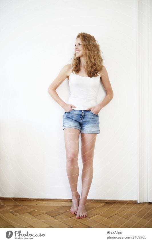 young redhead woman with curls and freckles stands barefoot in hot pants in front of white door and smiles Style Happy pretty Body Life Well-being