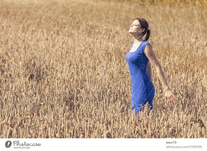 Beautiful young woman in autumn on corn field to the horizon. Pretty girl with zest for life enjoying the sunshine break and life. Rest and recharge energy from time stress in environment and nature idyll. Blue dress.