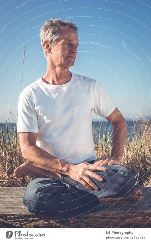 Man sitting in a relaxed yoga pose at the beach. Relaxation Meditation Sun Yoga Adults Old Sit Natural Power Serene 50-60 years Action color image