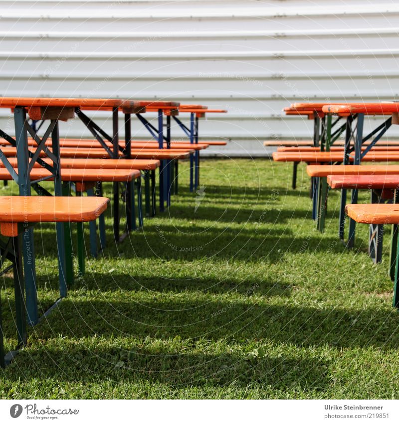Beer tent sets in sunlight in front of flight hall Beer table Bench Grass Meadow Wood Stand Empty Shadow Line Metal Colour photo Exterior shot Deserted Day