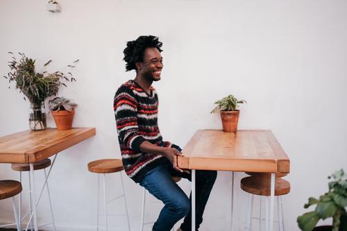 Young happy afro american man sitting in cafe Lifestyle Joy Relaxation Table Restaurant Human being Man Adults Youth (Young adults) Afro Wood Smiling Sit Modern