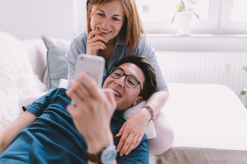 Mixe Race young adult couple watching video on phone House (Residential Structure) Living room Telephone Technology Couple Happiness asian girlfriend boyfriend