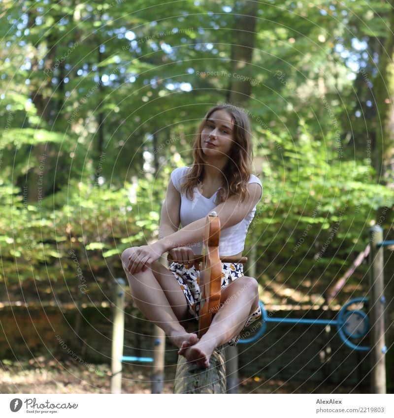 Young, athletic woman sits on a seesaw for children on a playground in the forest; she is barefoot and smiles at the camera Joy pretty Athletic Fitness