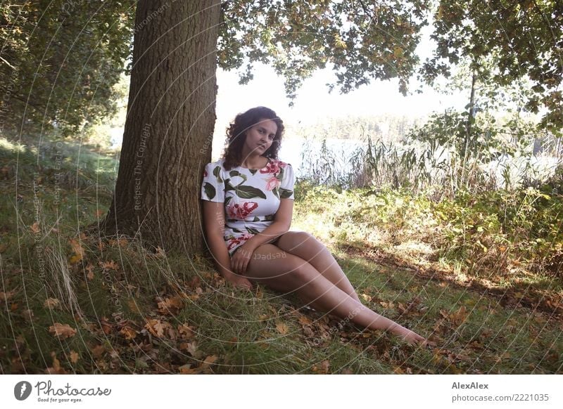 Full body image of tall beautiful woman with long dark curly hair in nature sitting barefoot under tree pretty Wellness Well-being Summer vacation Young woman