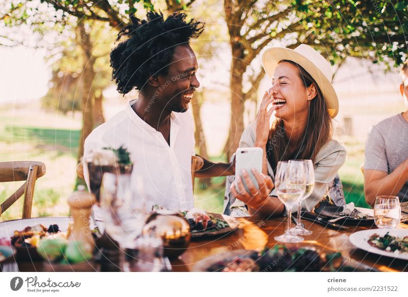 Mixed race couple having fun with phone at dinner party Lunch Dinner Alcoholic drinks Joy Happy Summer Sun Restaurant Feasts & Celebrations Telephone Technology