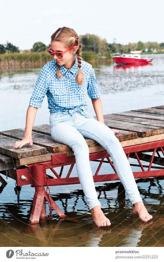 Young girl sitting on jetty over the lake and dipping feet in water on sunny day in the summertime Lifestyle Joy Happy Relaxation Leisure and hobbies