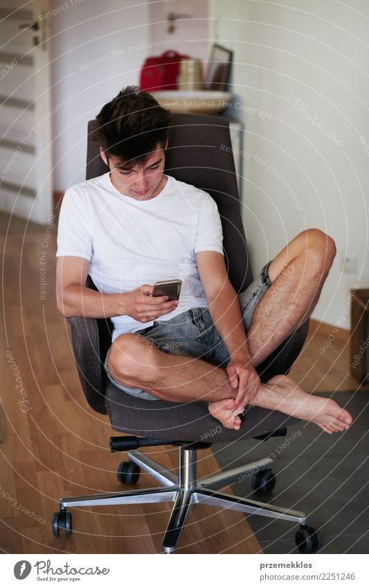 Relaxed boy chatting with friends using smart phone Lifestyle Happy Relaxation Chair Telephone Cellphone PDA Technology Human being Young man