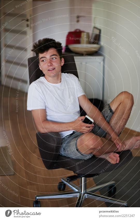 Relaxed boy holding smartphone sitting in chair at home Lifestyle Happy Relaxation Chair Telephone PDA Technology Human being Young man Youth (Young adults) Man