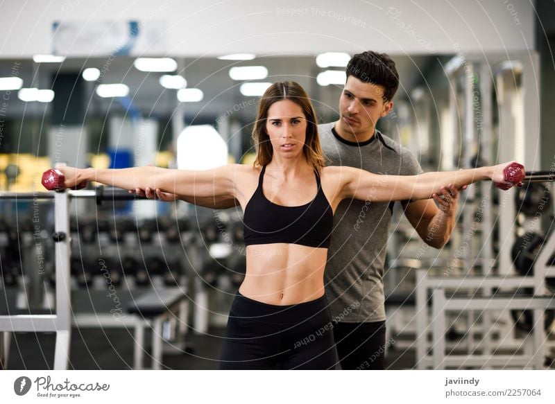 Personal trainer helping a young woman lift dumbells Lifestyle Body Sports Human being Masculine Feminine Young woman Youth (Young adults) Young man Woman