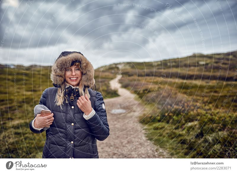 Middle-aged woman braving a cold winter in nature Happy Winter Telephone Cellphone Woman Adults Nature Landscape Sky Storm Wind Coat Smiling breezy walking