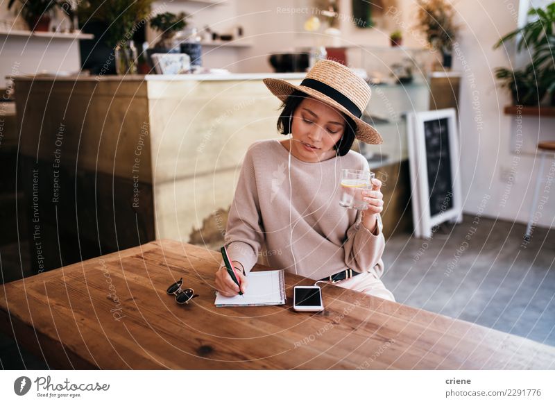 Asian young woman writing notes in notebook Drinking Table Music Work and employment Woman Adults Youth (Young adults) Musical notes Hat Paper Pen Listening Sit