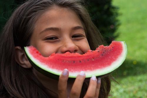 Smiling girl with a bitten melon in front of her mouth Joy Summer Garden Child Girl Infancy 1 Human being 8 - 13 years Brunette Eating Laughter Happiness Happy