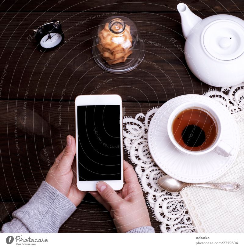 female hands holding a white smartphone Breakfast Beverage Tea Plate Mug Lifestyle Table Telephone PDA Screen Technology Woman Adults Arm Hand 1 Human being
