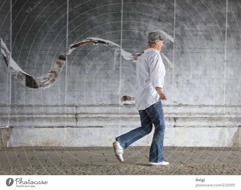 Woman with cap in jeans and white shirt walking along a wall Human being Adults Female senior Life 1 45 - 60 years Tunnel Wall (barrier) Wall (building)