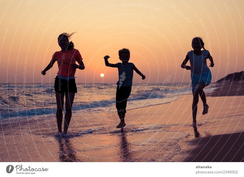 Happy children playing on the beach at the sunset time. Three Kids having fun outdoors. Concept of summer vacation and friendly family. Lifestyle Joy