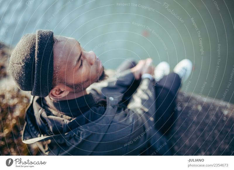 Young man sitting on the habour looking down the water Lifestyle Human being Youth (Young adults) 13 - 18 years 18 - 30 years Adults Spring Bad weather Wind Hat
