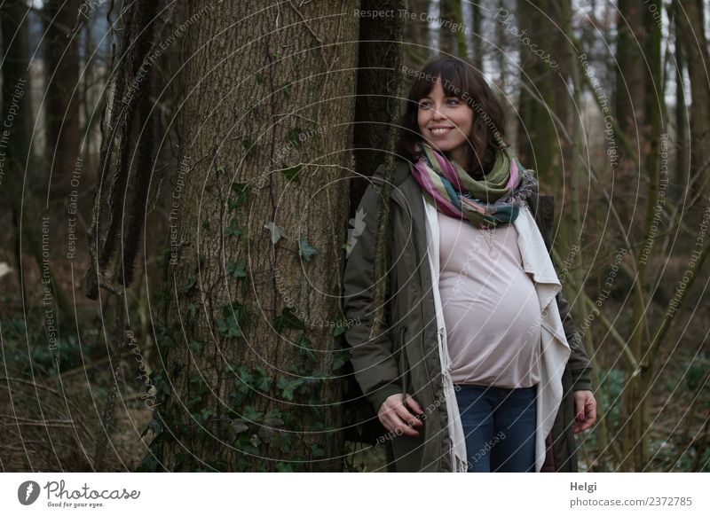 young pregnant woman stands smiling at a tree Human being Feminine Young woman Youth (Young adults) Adults 1 30 - 45 years Environment Nature Tree Forest