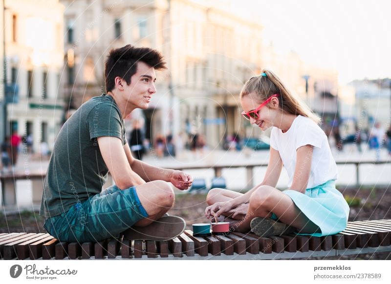 Young teenage girl and boy spending time together in the city centre enjoy eating ice cream on a summer day. Spending quality time on sunny afternoon eating sweet dessert. Downtown area in the background