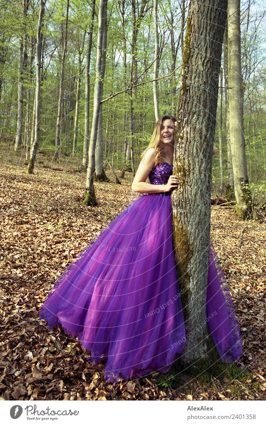 Young tall beautiful woman in purple wedding dress leans against tree in forest and laughs Lifestyle Elegant Style pretty Young woman Youth (Young adults)