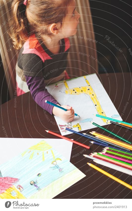 Little girl drawing the colorful pictures of giraffe and playing children using pencil crayons sitting at table indoors. Shot from above Lifestyle Joy Happy