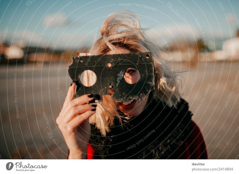 Smiling blonde girl holding an old broken video tape in the hand and looking through the holes at sunset. Leisure and hobbies Film maker Human being Young woman