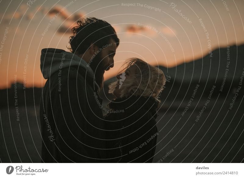 Blonde girl and bearded man hugging to each other at dusk, with orange sky in the background. Lifestyle Leisure and hobbies Tourism Freedom Human being