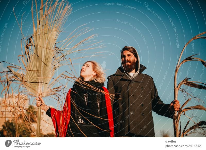 Blonde woman and bearded man posing with plant branches in the hand at sunset, and blue sky in the background. Lifestyle Joy Leisure and hobbies Summer