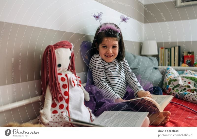 Little girl disguised as butterfly sitting on bed while reading book Lifestyle Happy Beautiful Playing Reading Lamp Bedroom Child Human being Woman Adults