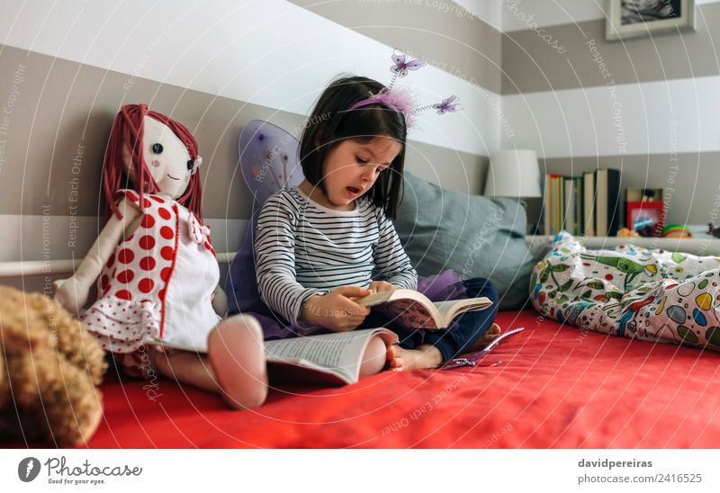 Little girl disguised sitting on bed reading a book Lifestyle Beautiful Playing Reading Bedroom Child School To talk Human being Woman Adults Friendship Book