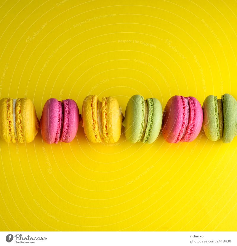 macarons lies in a row in the middle Dessert Candy Eating Bright Yellow Green Pink Colour Idea Macaron background food colorful Vanilla french cake
