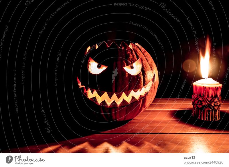 Creepy carved Halloween pumpkin next to burning candle Hallowe'en Head Eyes Mouth Art Nature Autumn Glittering Smiling Laughter Illuminate Aggression Old Threat